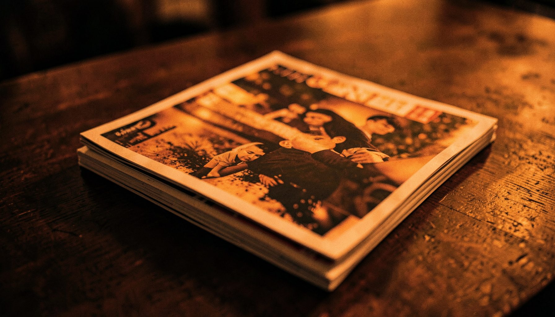 Stack of music magazines on a dark wooden surface, warm amber light casting soft shadows, editorial mood