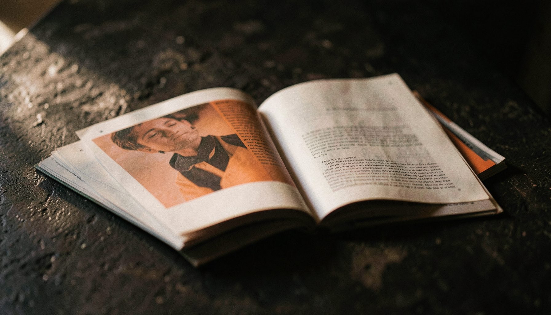 Open magazine pages on a textured dark surface, soft natural light from the side, contemplative editorial mood