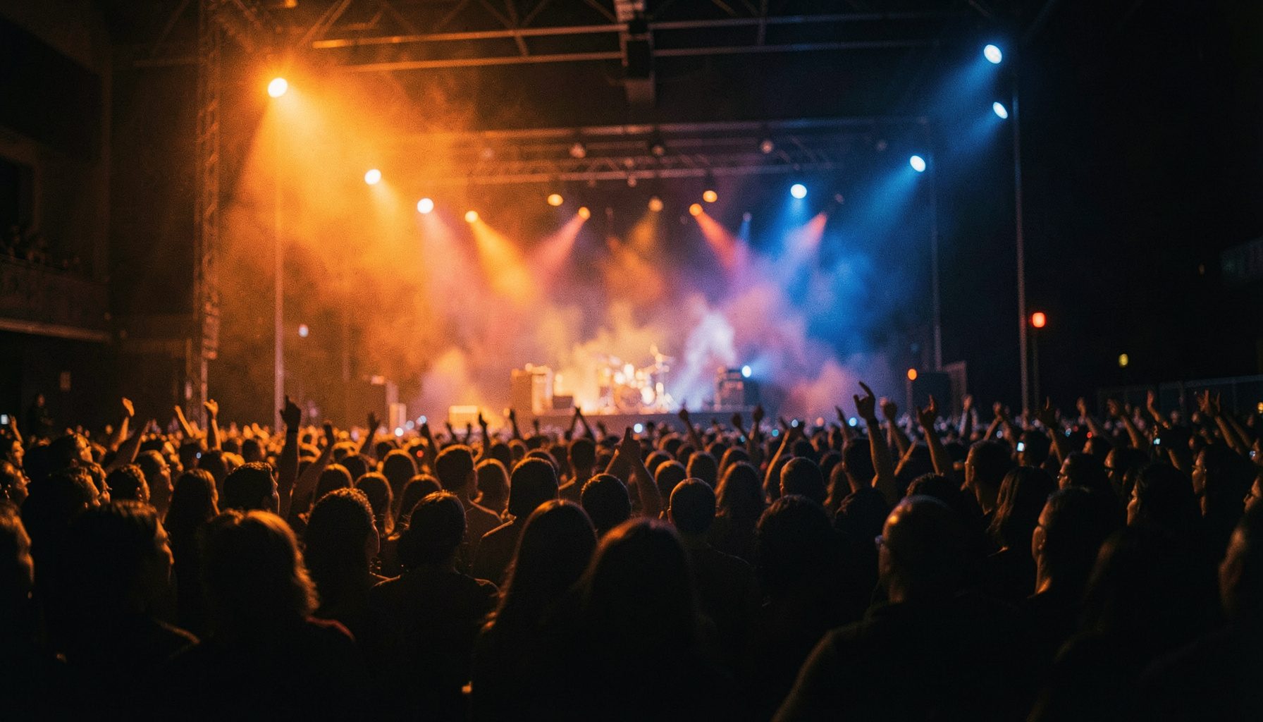 Dimly lit concert stage with warm amber and deep blue lighting, wide cinematic frame, shallow depth of field, atmospheric crowd silhouettes