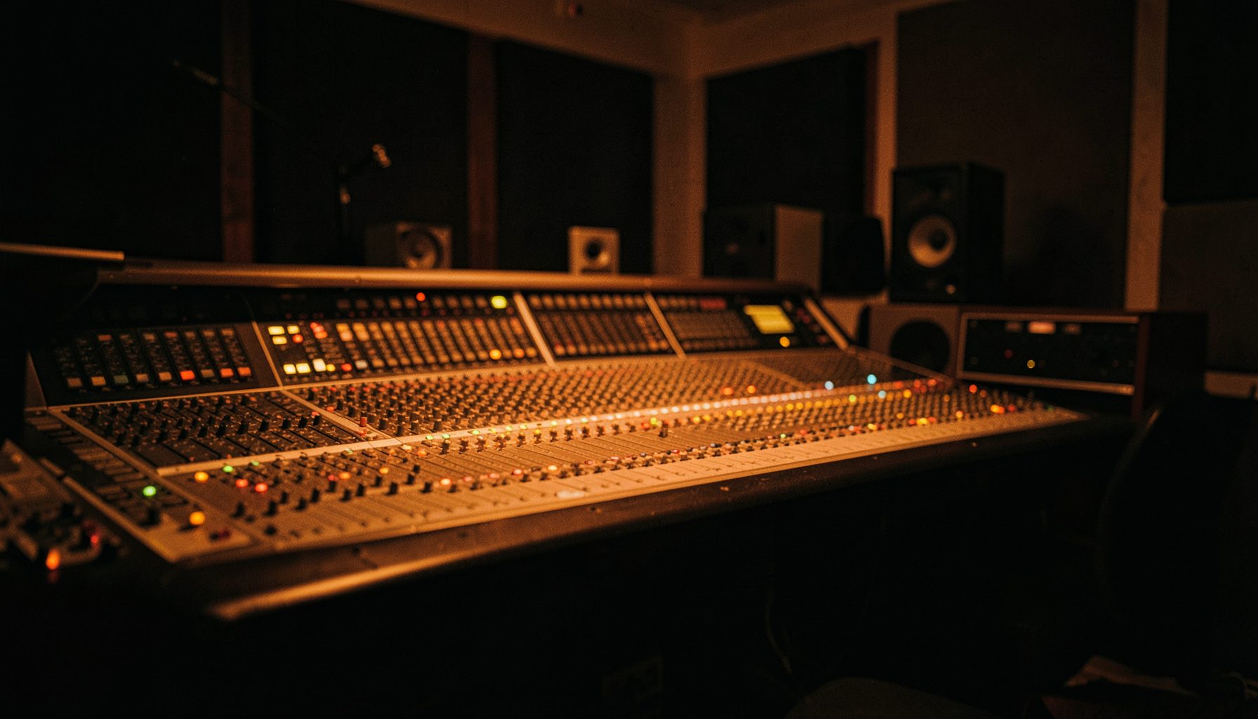 A dimly lit recording studio control room with mixing console and warm amber glow, deep shadows across the equipment, cinematic wide frame