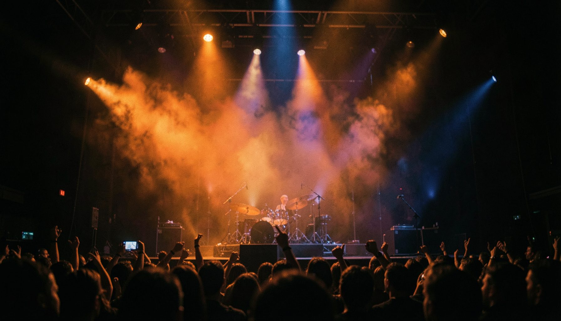 Dimly lit concert stage with warm amber and deep blue spotlights cutting through haze, wide cinematic frame with shallow depth of field