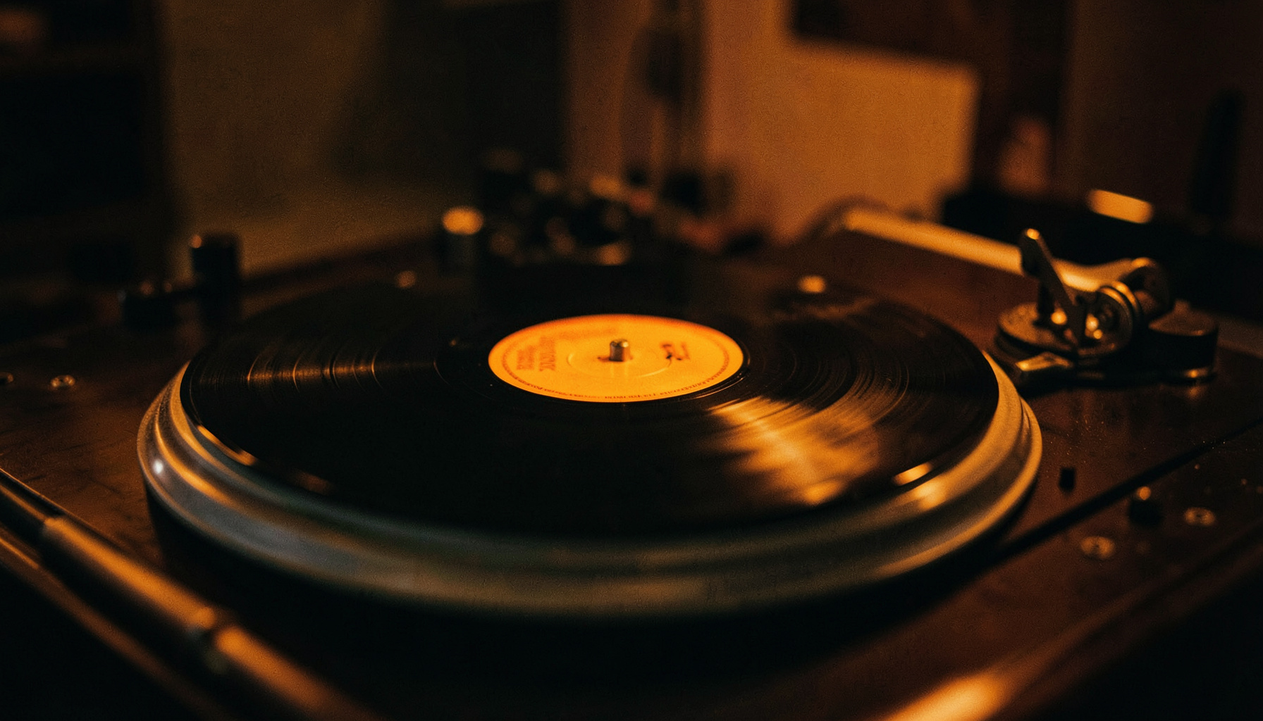 Dimly lit vinyl record on a turntable with warm amber and deep charcoal tones, shallow depth of field, cinematic atmosphere